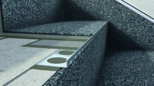 Aluminiowy profil schodowy zamontowany w posadzce żywicznej, zapewniający estetyczne wykończenie krawędzi stopnia i ochronę narożnika.
